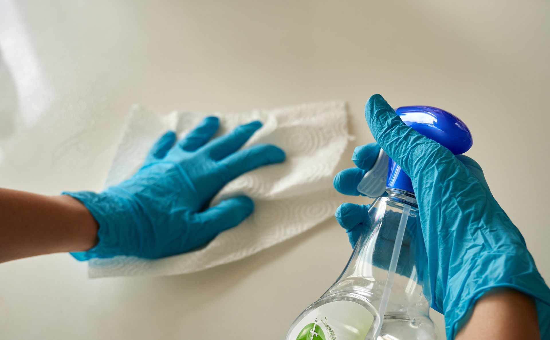 A Person Wearing Blue Gloves is Cleaning a Table With a Towel and Spray Bottle