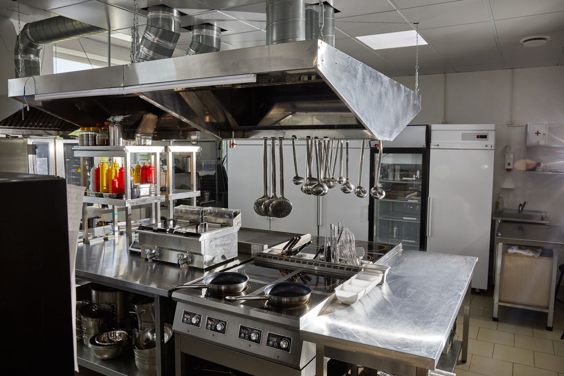 A Large Commercial Kitchen With Stainless Steel Appliances and Utensils Hanging From the Ceiling
