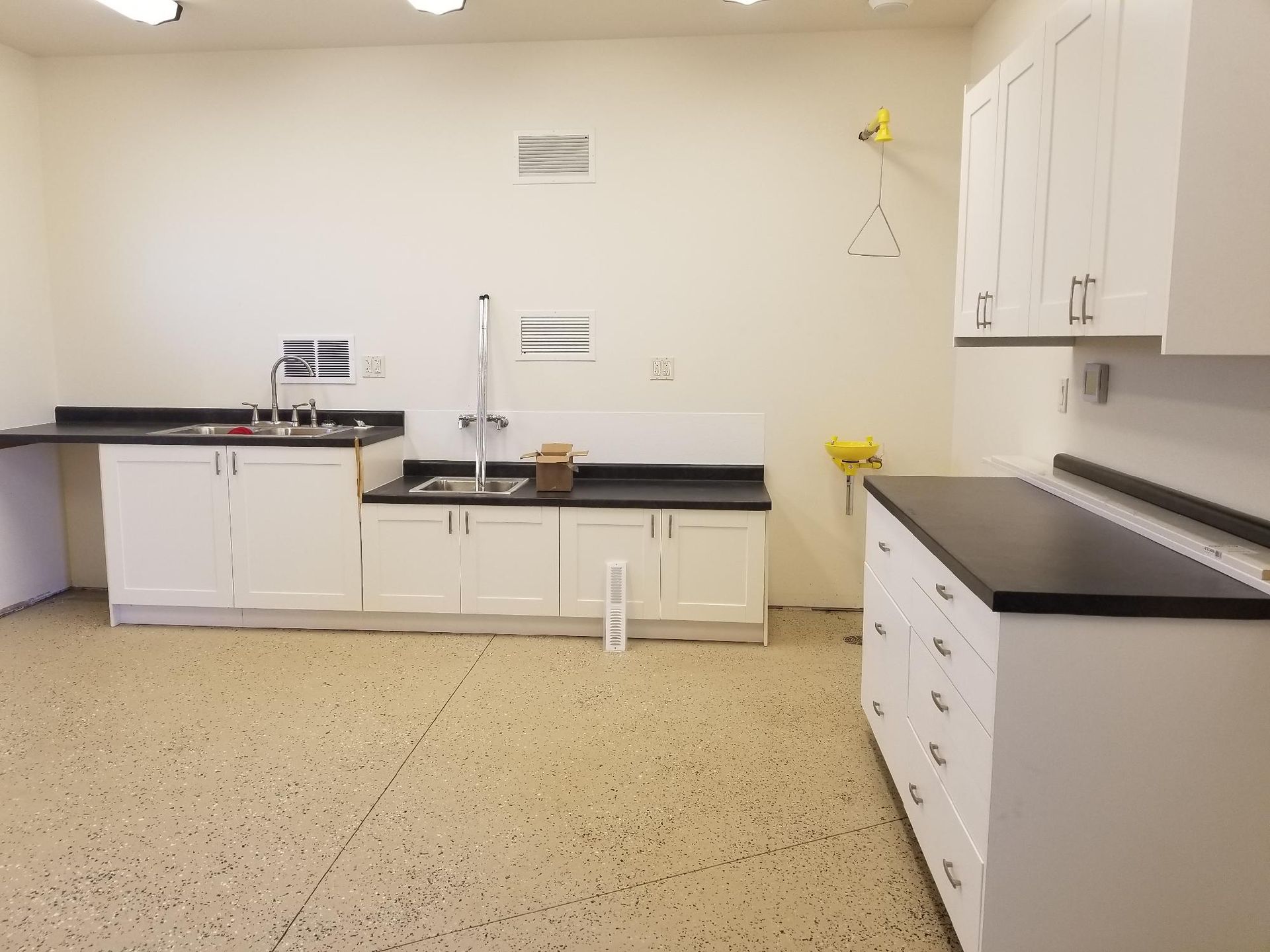 A medical exam room with white cabinets, dark countertops, a sink, and a speckled floor.