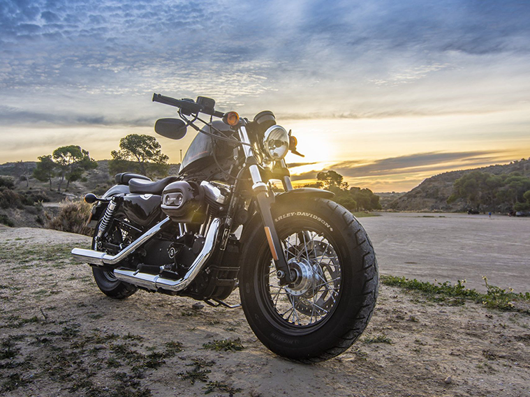 A motorcycle is parked on the side of a dirt road at sunset.