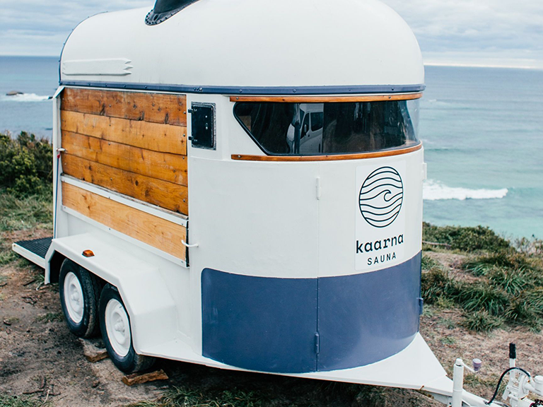 A trailer is parked on top of a grassy hill near the ocean.