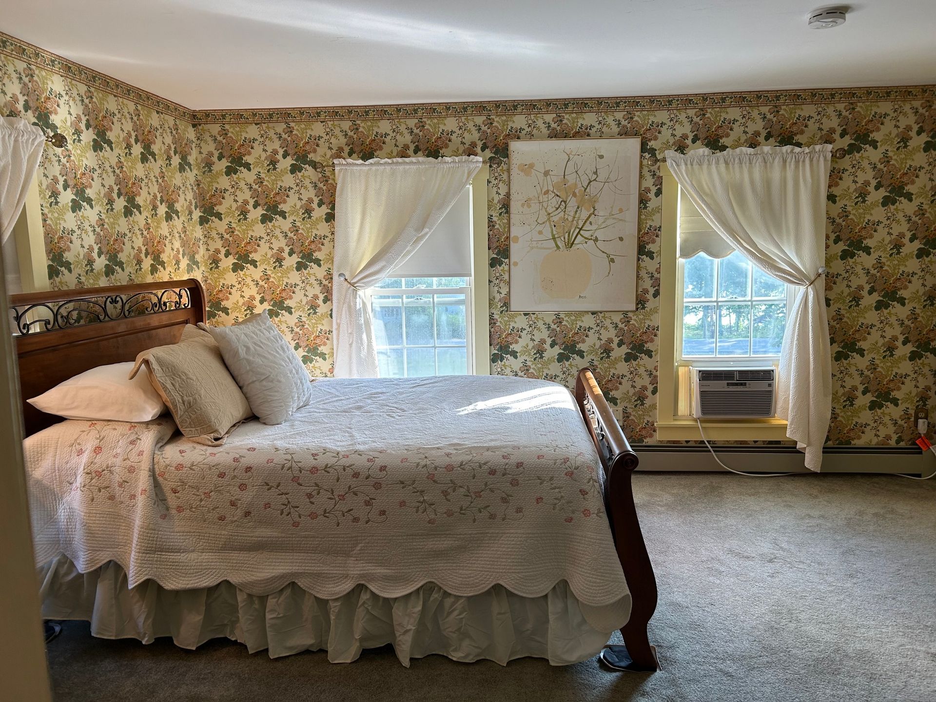 Floral wallpaper bedroom with a bed, white curtains, and a window air conditioner under the right window