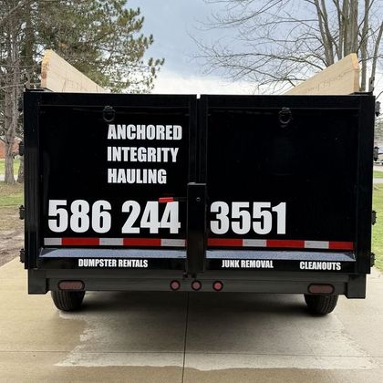 Back of a black dump trailer for Anchored Integrity Hauling with phone number 586-244-3551 and services listed.