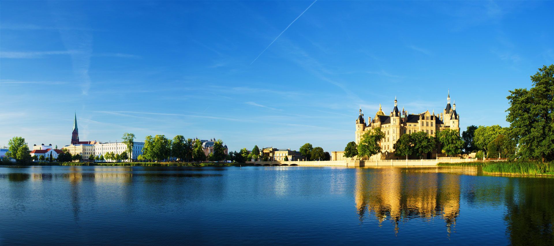 Ein großes Schloss spiegelt sich im Wasser eines Sees.
