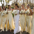Bridesmaids in pale yellow dresses walk with a bride in a white gown outdoors, holding bouquets.