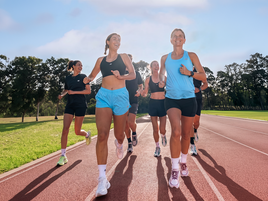 Runners jogging on a track in bright daylight, with trees and grass in the background