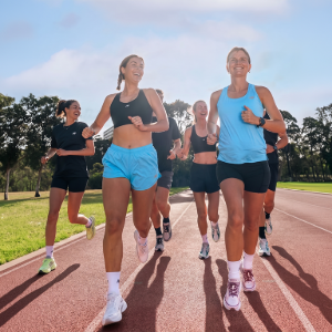 Runners jogging on a track in daylight, led by two women in blue and black athletic wear