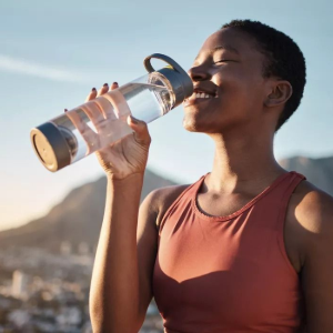 Woman drinking from a clear water bottle outdoors at sunrise