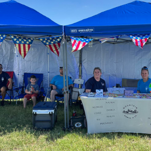 Blue tents at an outdoor event with people seated behind a registration table and patriotic bunting.