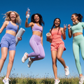 Four friends jumping and smiling in colorful activewear against a clear blue sky