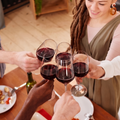 Friends clink glasses of red wine over a dinner table in a cozy indoor setting.