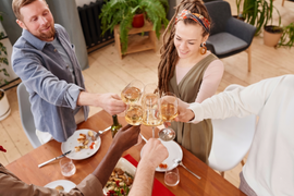 Friends toasting with drinks around a dining table in a bright home dining room