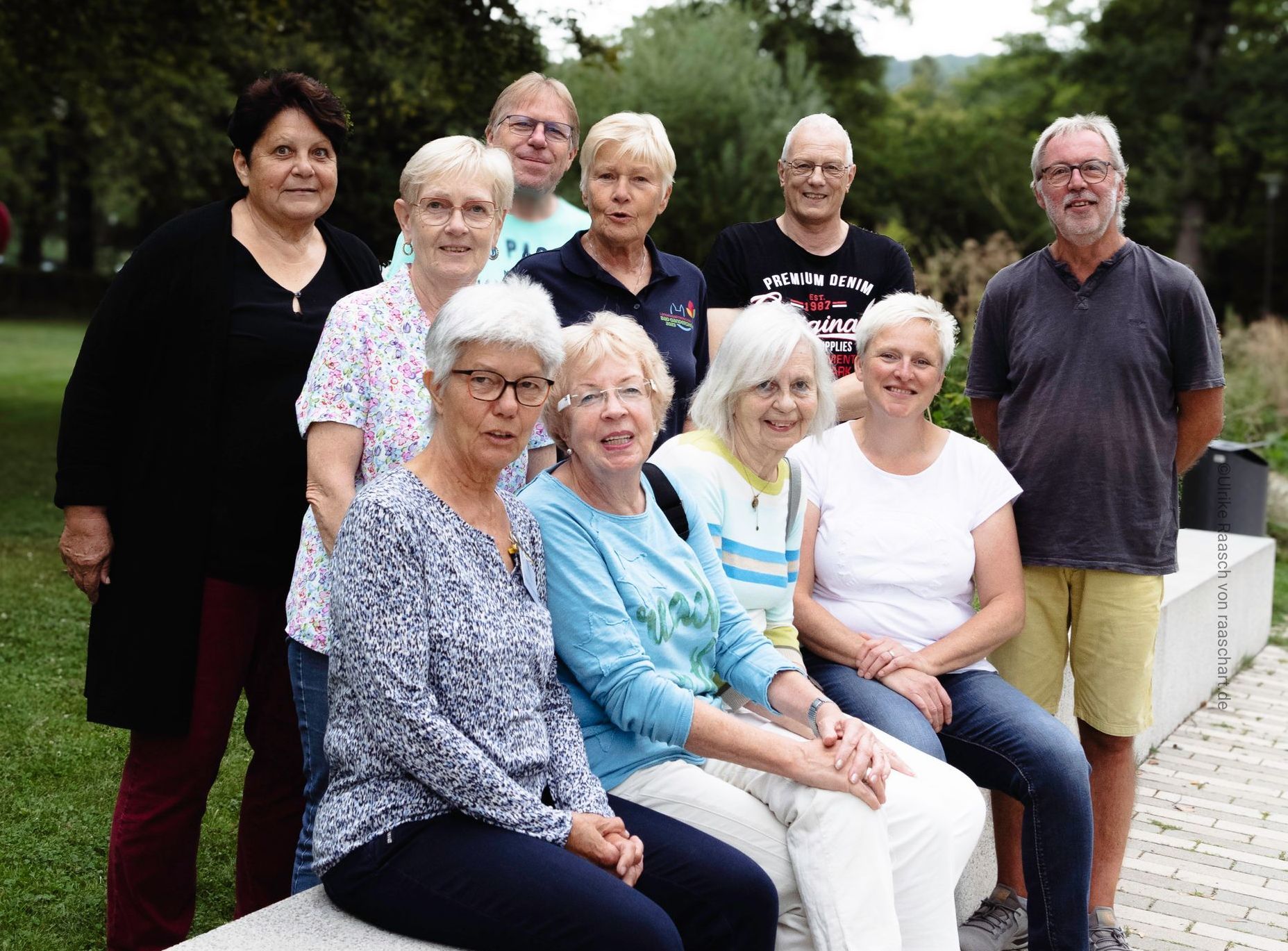 photo by www.raaschart.de Eine Gruppe lächelnder Menschen posiert im Freien. Mehrere Frauen in der ersten Reihe. Grasbewachsener Hintergrund.