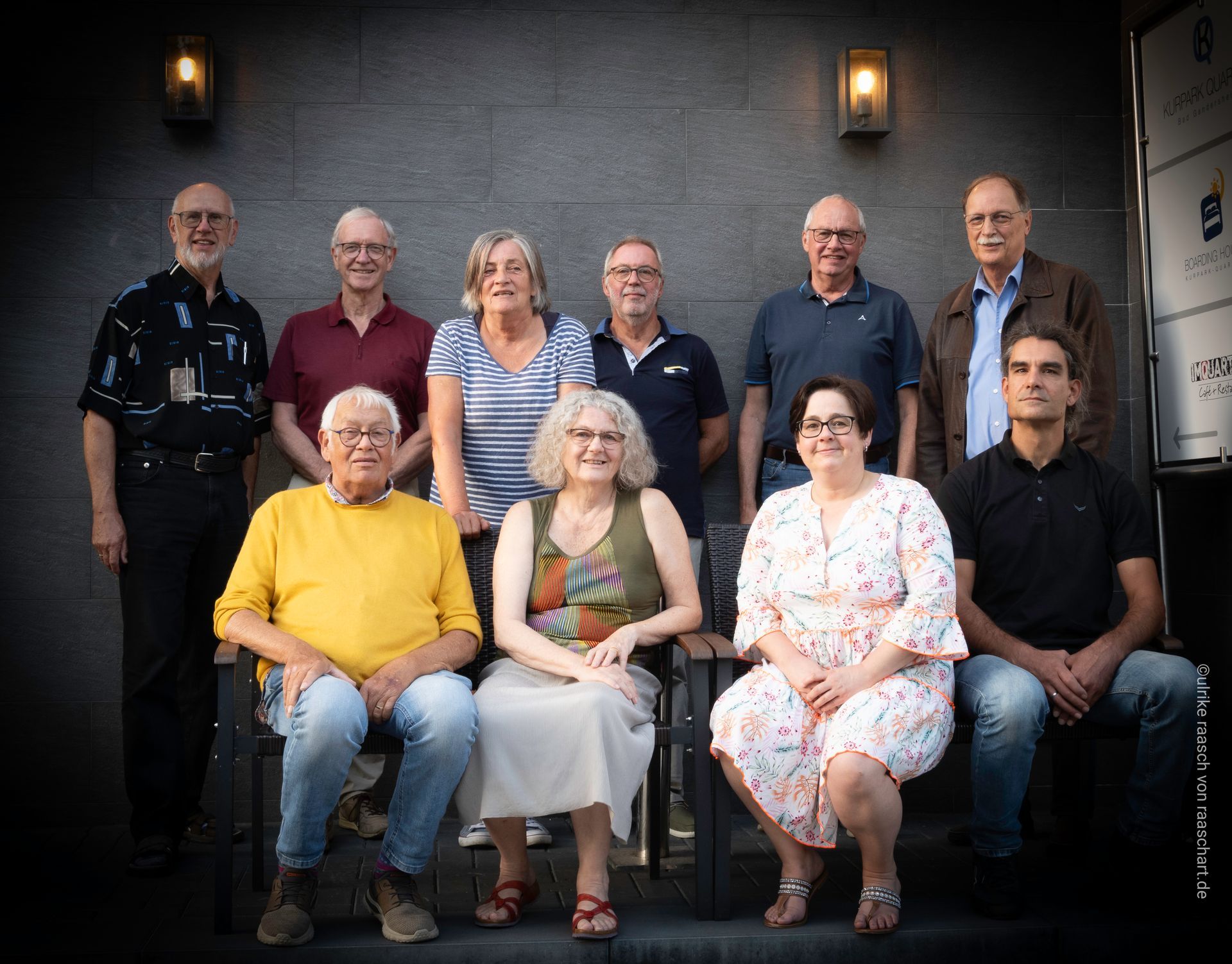 Eine Gruppe von Menschen posiert im Freien; einige sitzen, andere stehen in der Nähe eines Gebäudes mit Laternen.