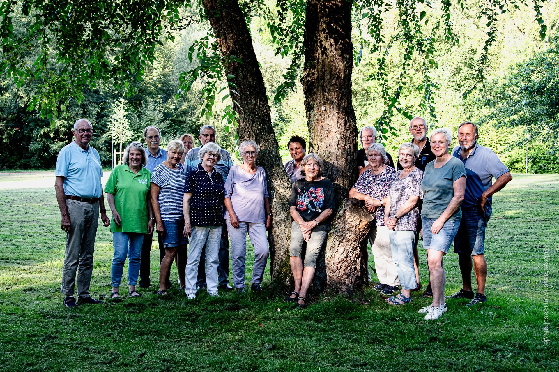 Eine Gruppe von Menschen steht in einem Park um einen großen Baum herum.