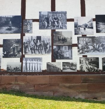 Wandpräsentation alter Schwarzweißfotos an einer Backstein- und Holzkonstruktion.