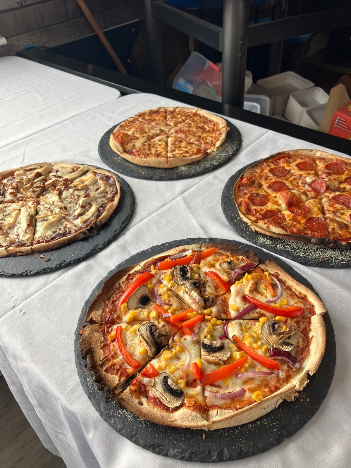 Vier Pizzen auf einem Tisch, jede mit unterschiedlichem Belag und serviert auf schwarzen Steinplatten.