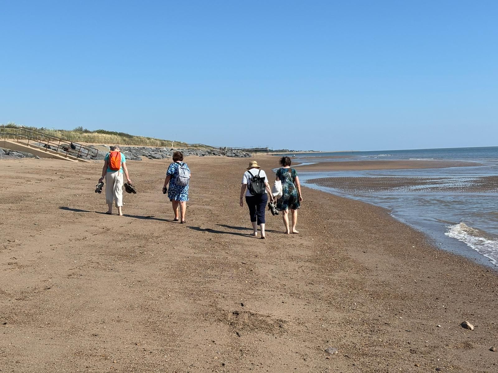 Vier Personen spazieren an einem sonnigen Tag an einem Sandstrand entlang.