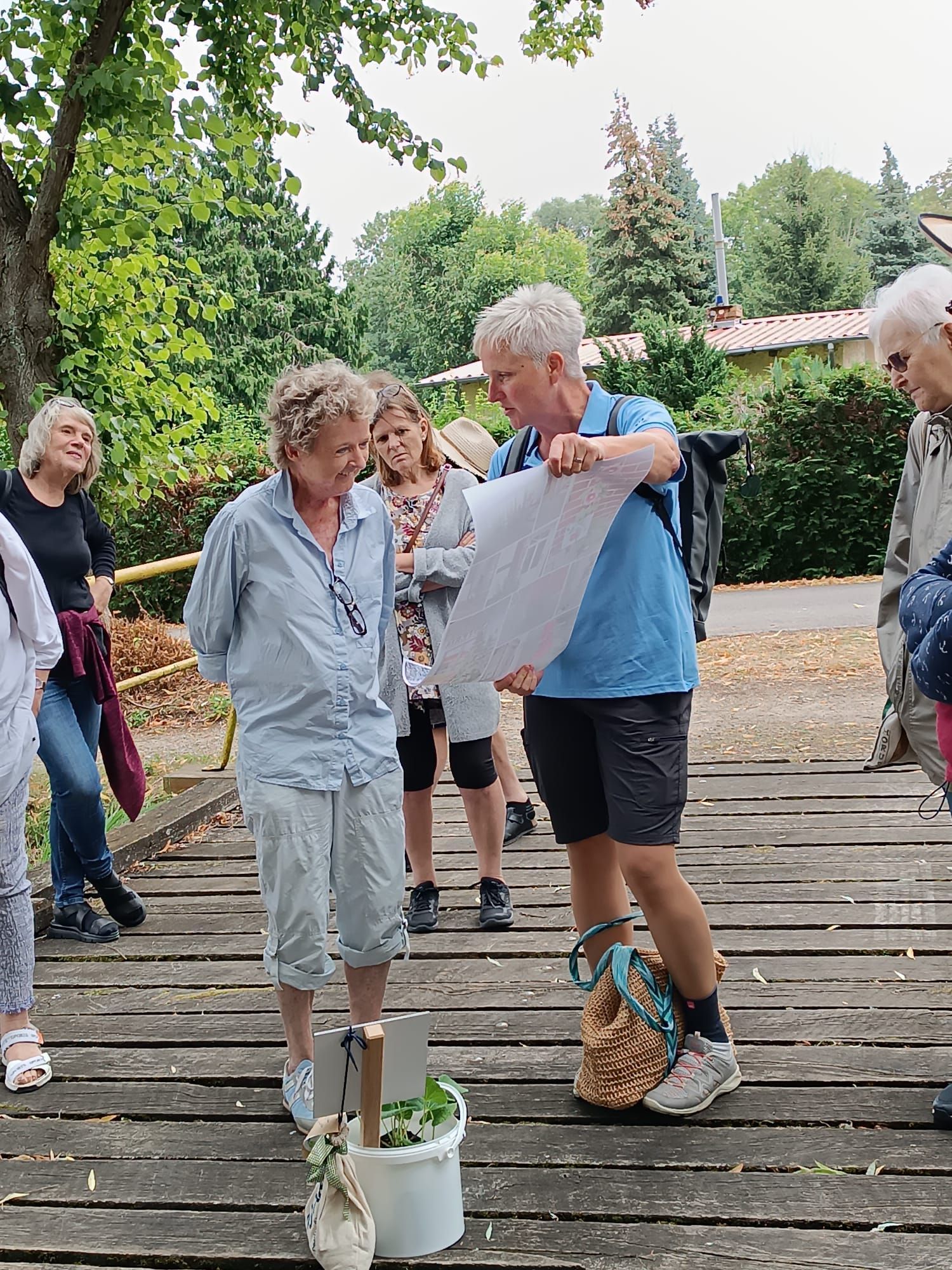 Eine Gruppe von Menschen auf einer Holzbrücke betrachtet eine Karte und unterhält sich im Freien darüber.