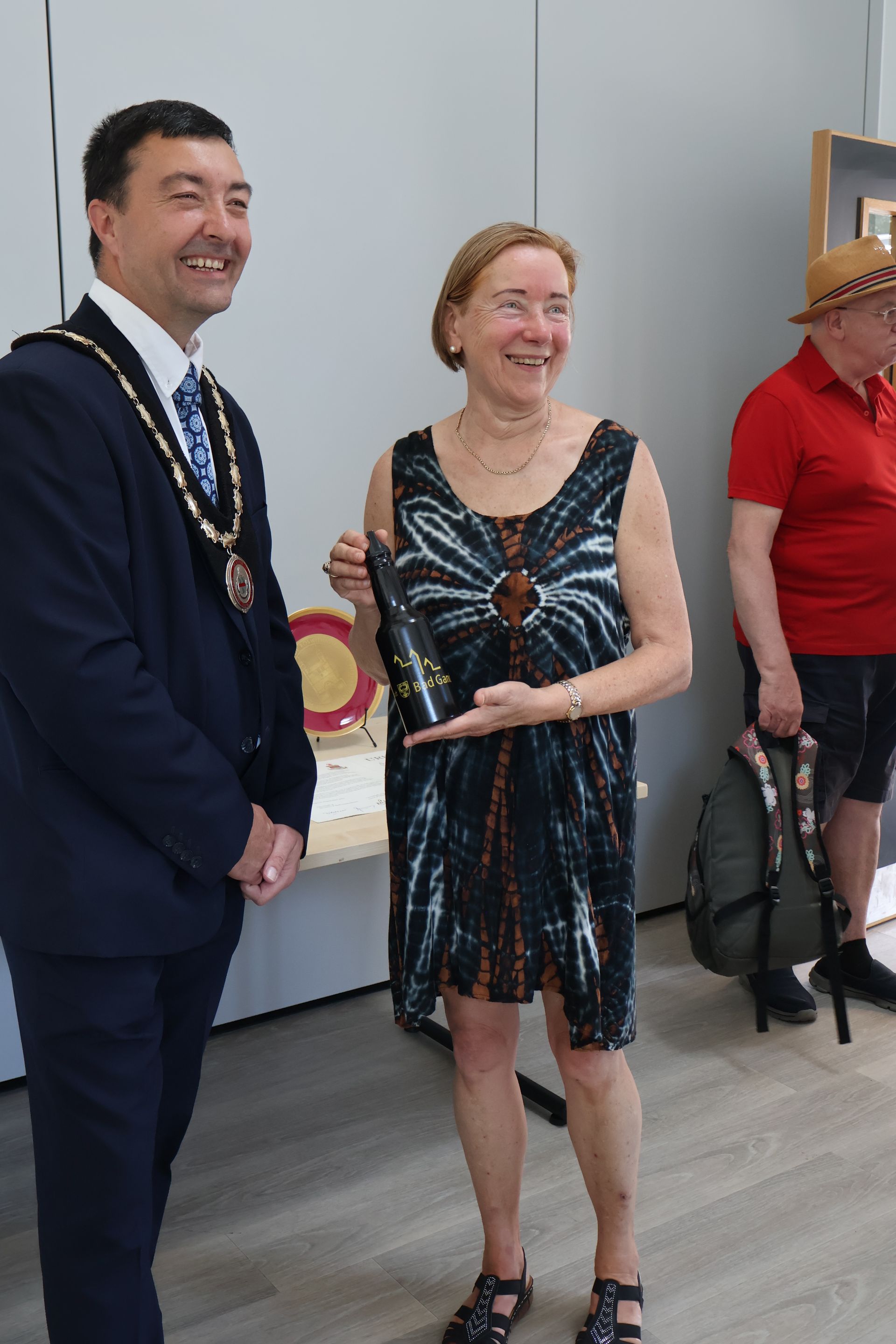 Ein Mann im Anzug und eine Frau im Kleid lächeln; die Frau hält eine Auszeichnung in der Hand.