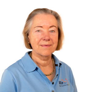 Woman in blue shirt, gold necklace, smiling slightly. Logo on shirt: 