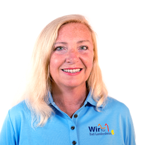 Eine Frau mit blonden Haaren und einem blauen Hemd lächelt in die Kamera.