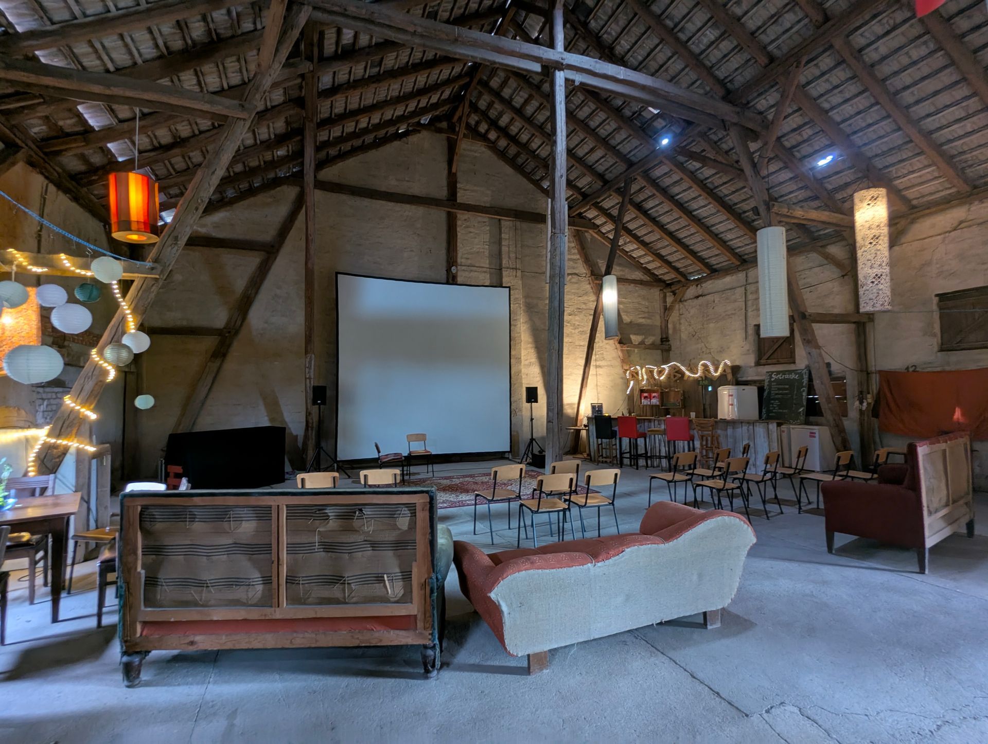 Innenausstattung einer Scheune für eine Filmvorführung. Weiße Leinwand, Sitzgelegenheiten und dekorative Beleuchtung.