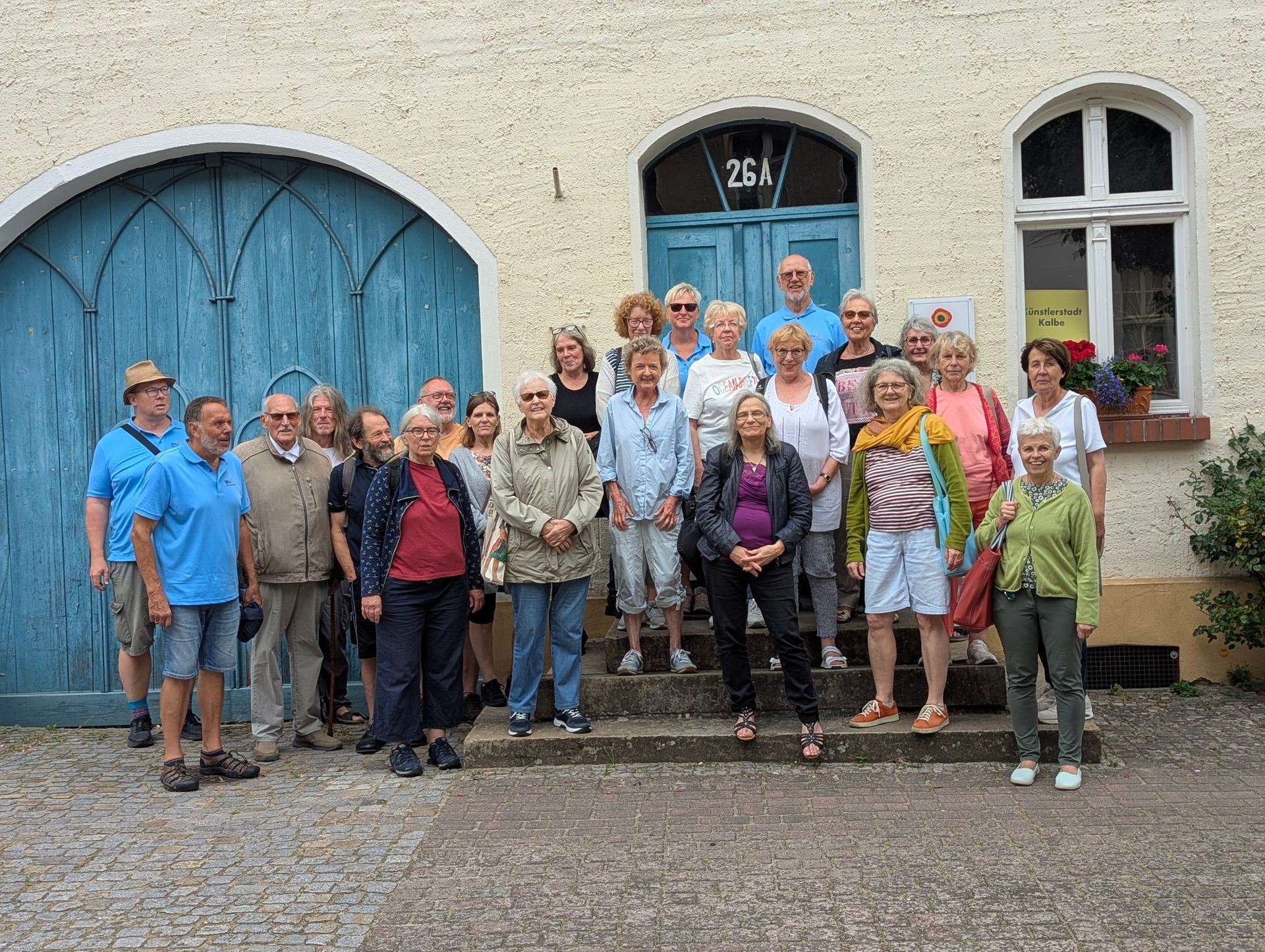 Eine Gruppe von Menschen steht auf Stufen vor einem Gebäude mit blauen Türen.