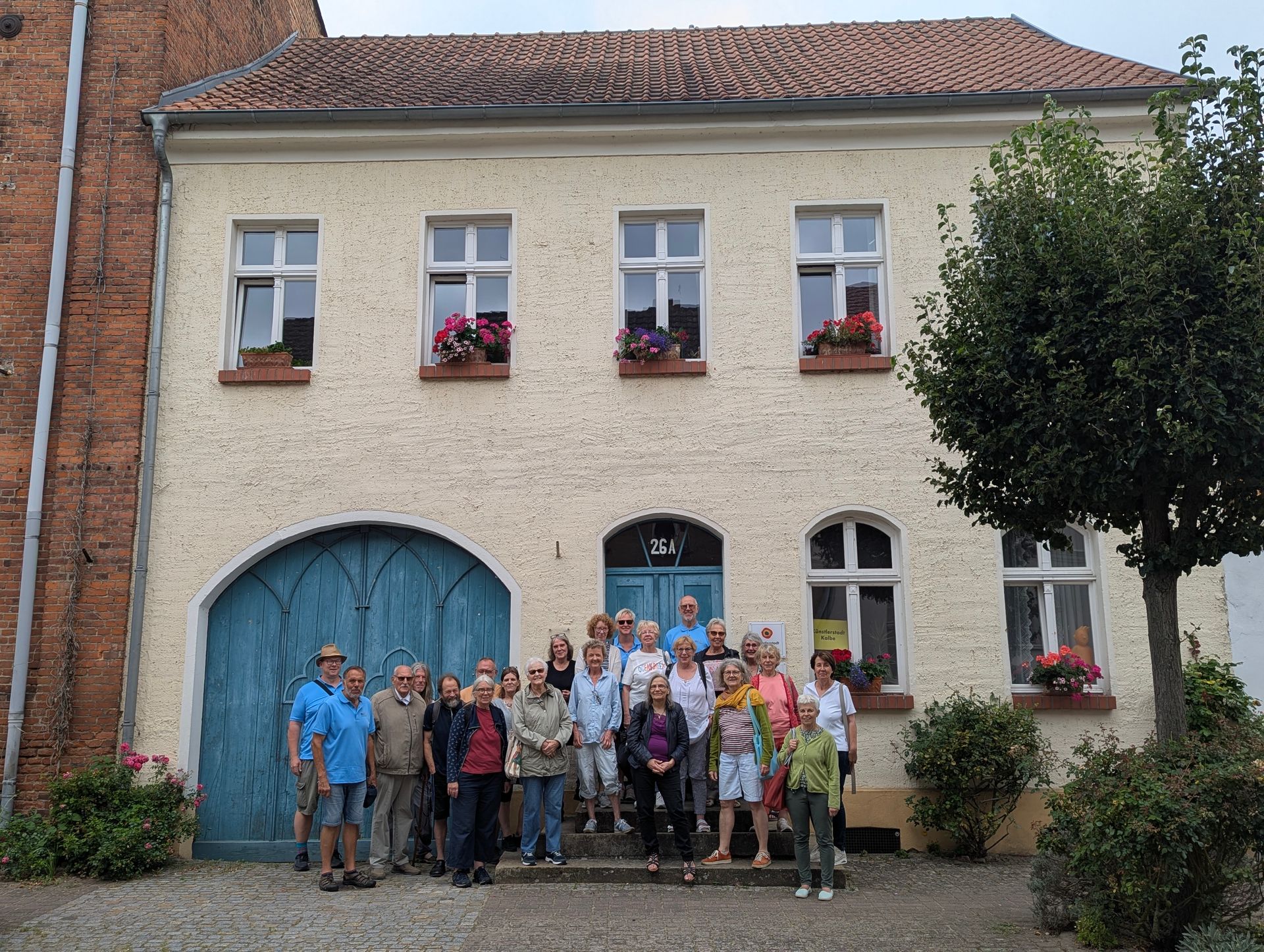 Eine Gruppe von Menschen steht vor einem hellgelben Gebäude mit blauen Türen und Fenstern.