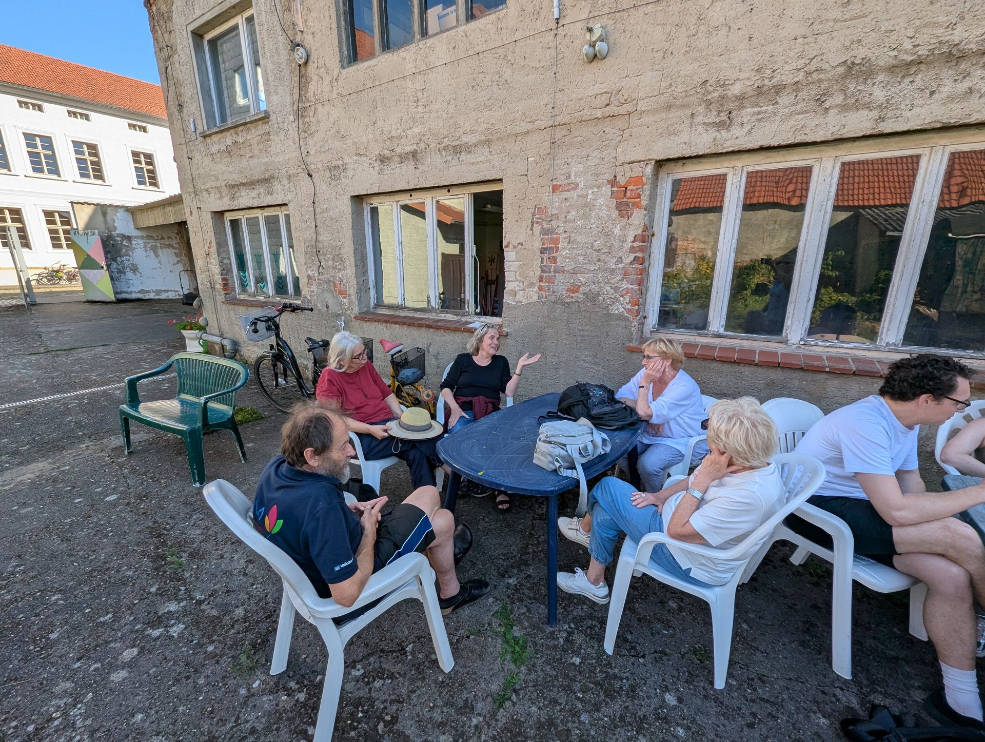 Eine Gruppe von Menschen sitzt draußen an einem Tisch in der Nähe eines Gebäudes.