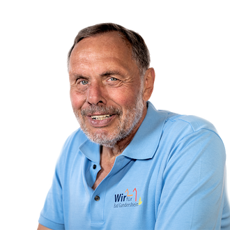 Mann in blauem Poloshirt lächelt, Logo links, vor weißem Hintergrund.