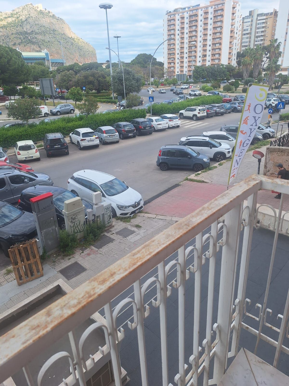 Vista dal balcone su un parcheggio, una strada e alti palazzi residenziali vicino a una montagna.