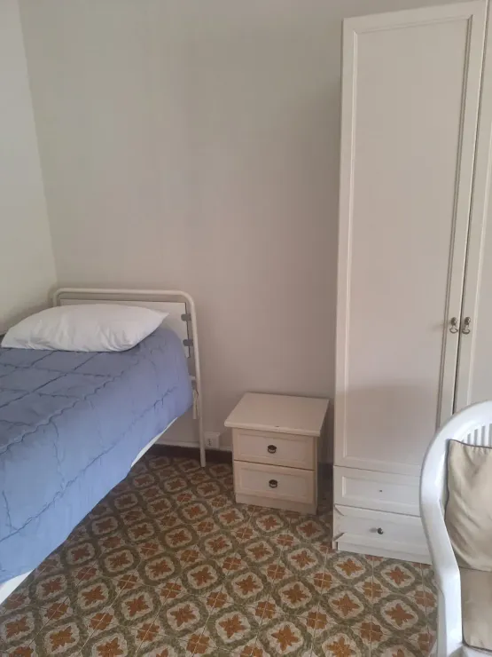 Piccola camera da letto con letto singolo, comodini, armadio bianco e pavimento piastrellato con motivi decorativi.