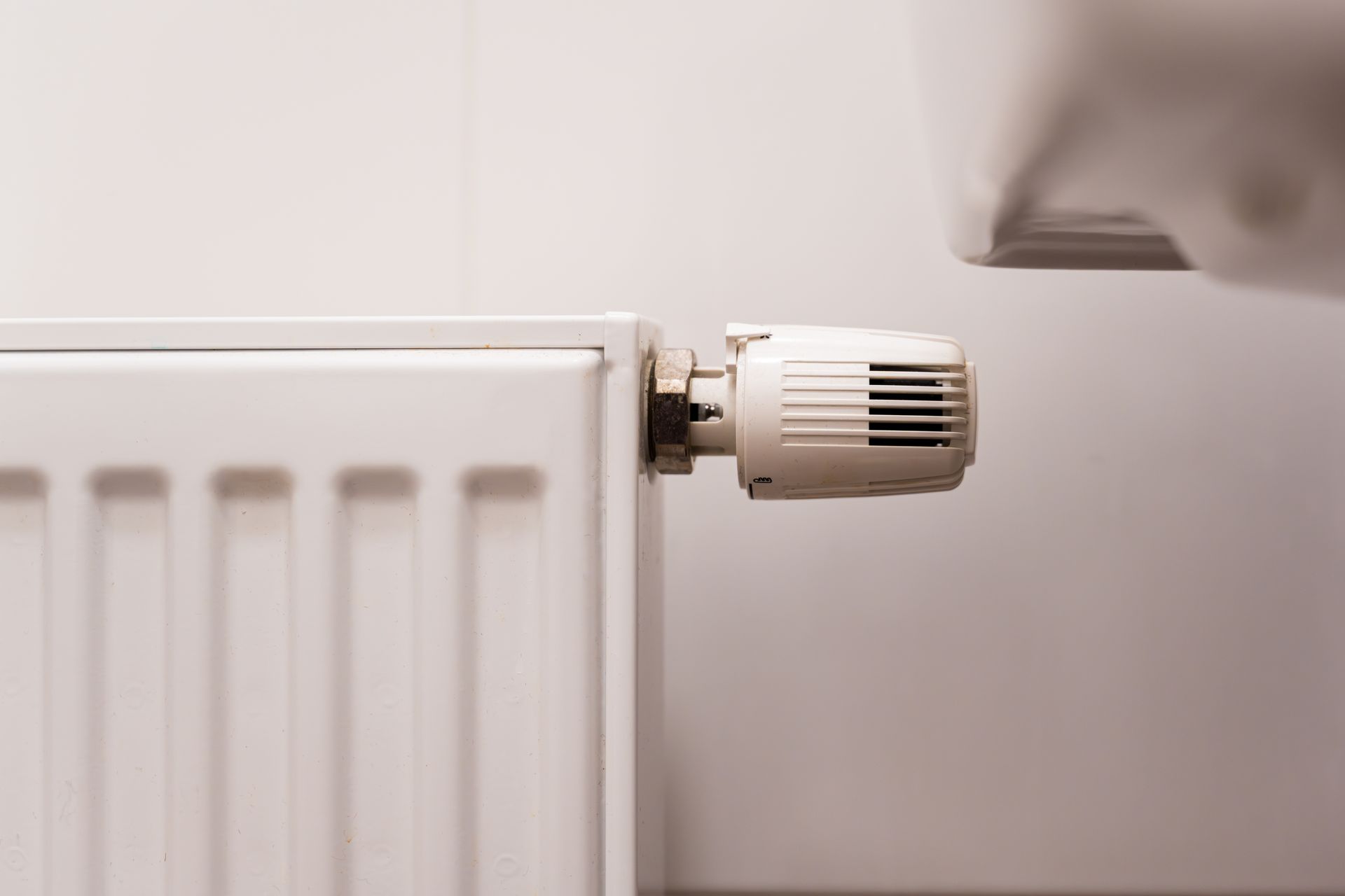 White radiator with a thermostatic valve against a light wall, with part of a window in view