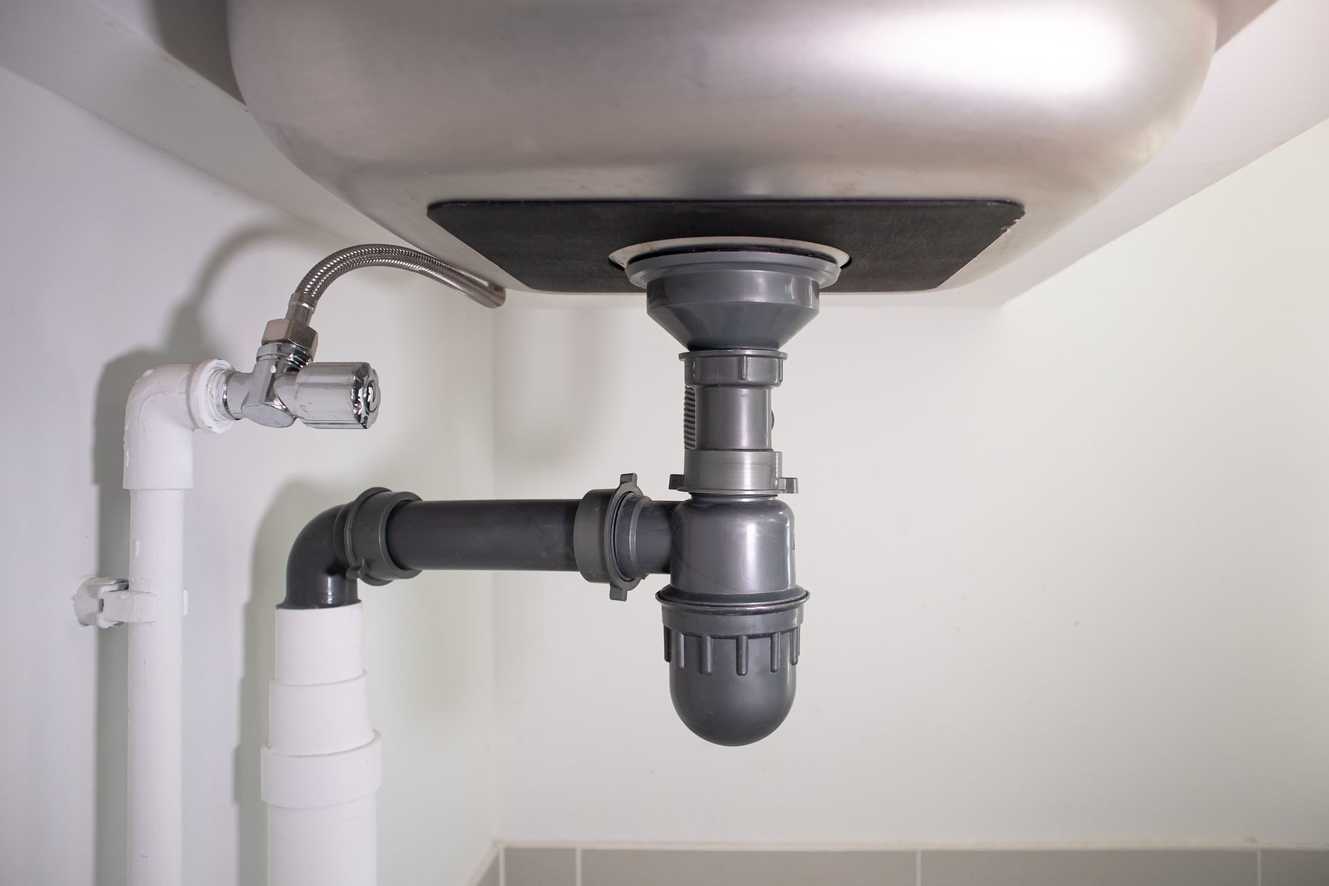 Under-sink plumbing with a gray drain pipe and white water lines in a cabinet