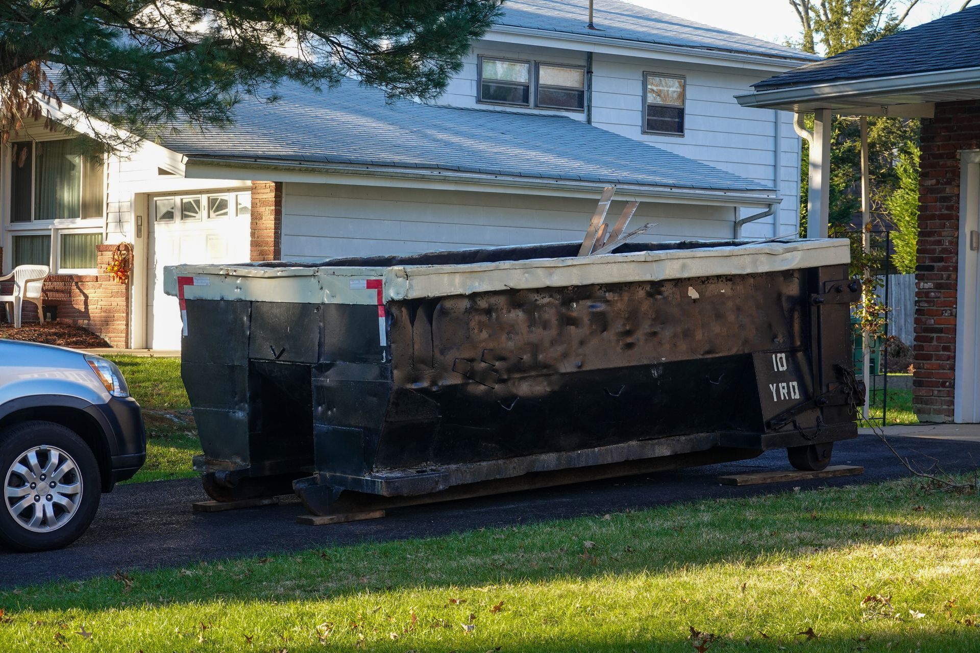 Large residential dumpster on a driveway in front of a suburban home for waste removal.