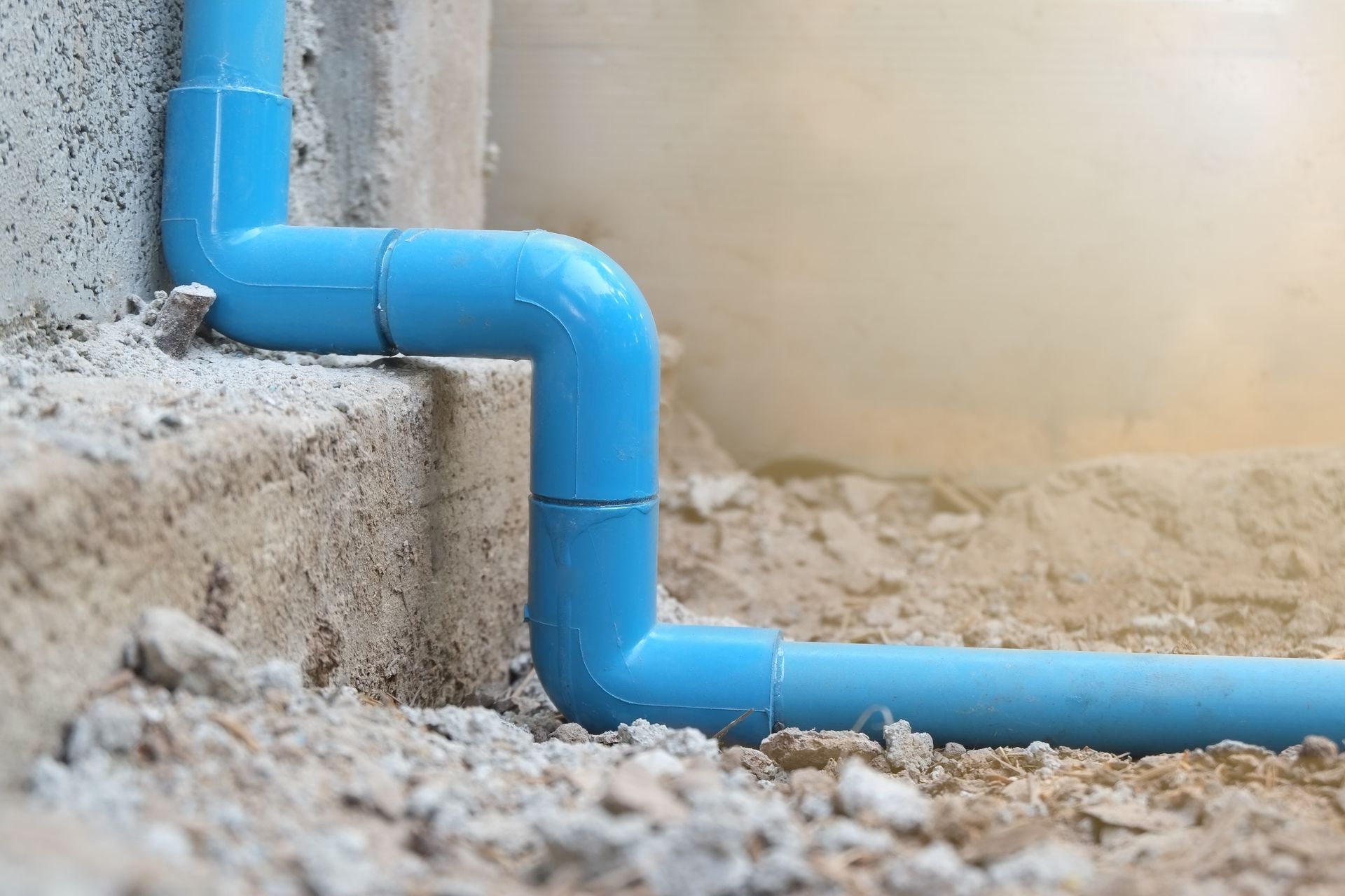Blue PVC pipe elbow joints beside a concrete wall in a dirt trench
