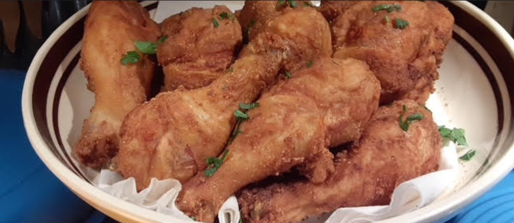 Bowl of fried chicken drumsticks, golden brown and garnished with herbs