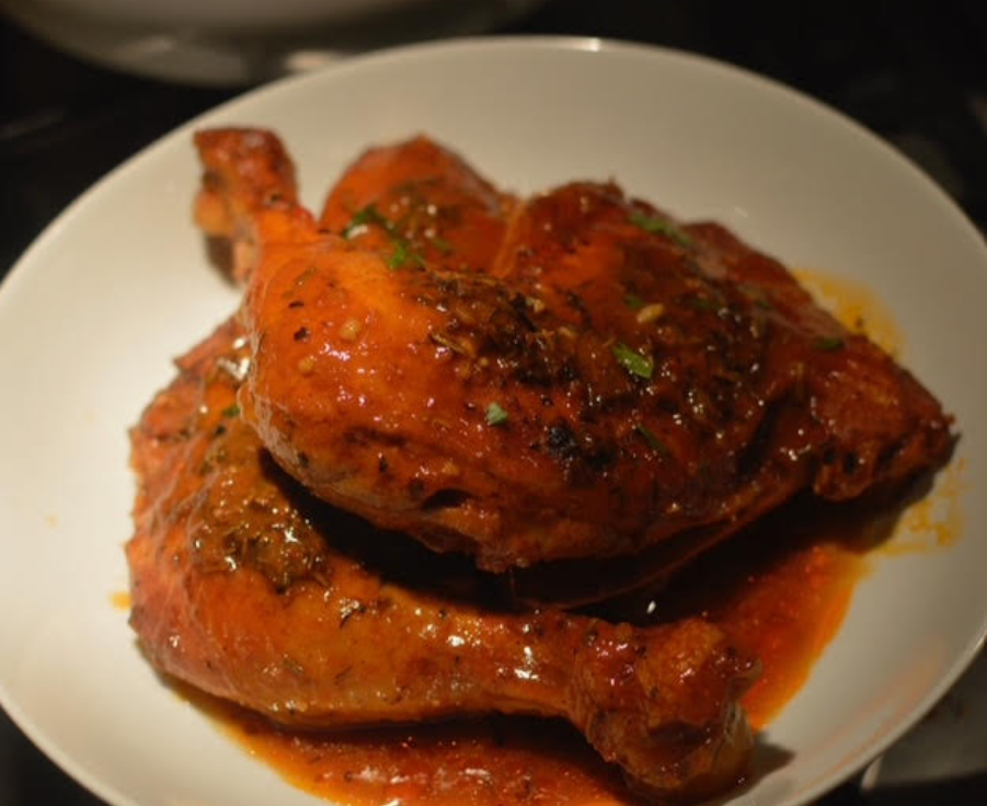 Two glazed roasted chicken legs on a white plate, coated in a reddish-brown sauce