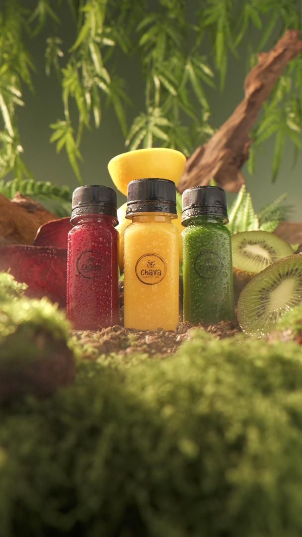 Three colorful juice bottles on a bed of moss, with fruit and foliage in the background.