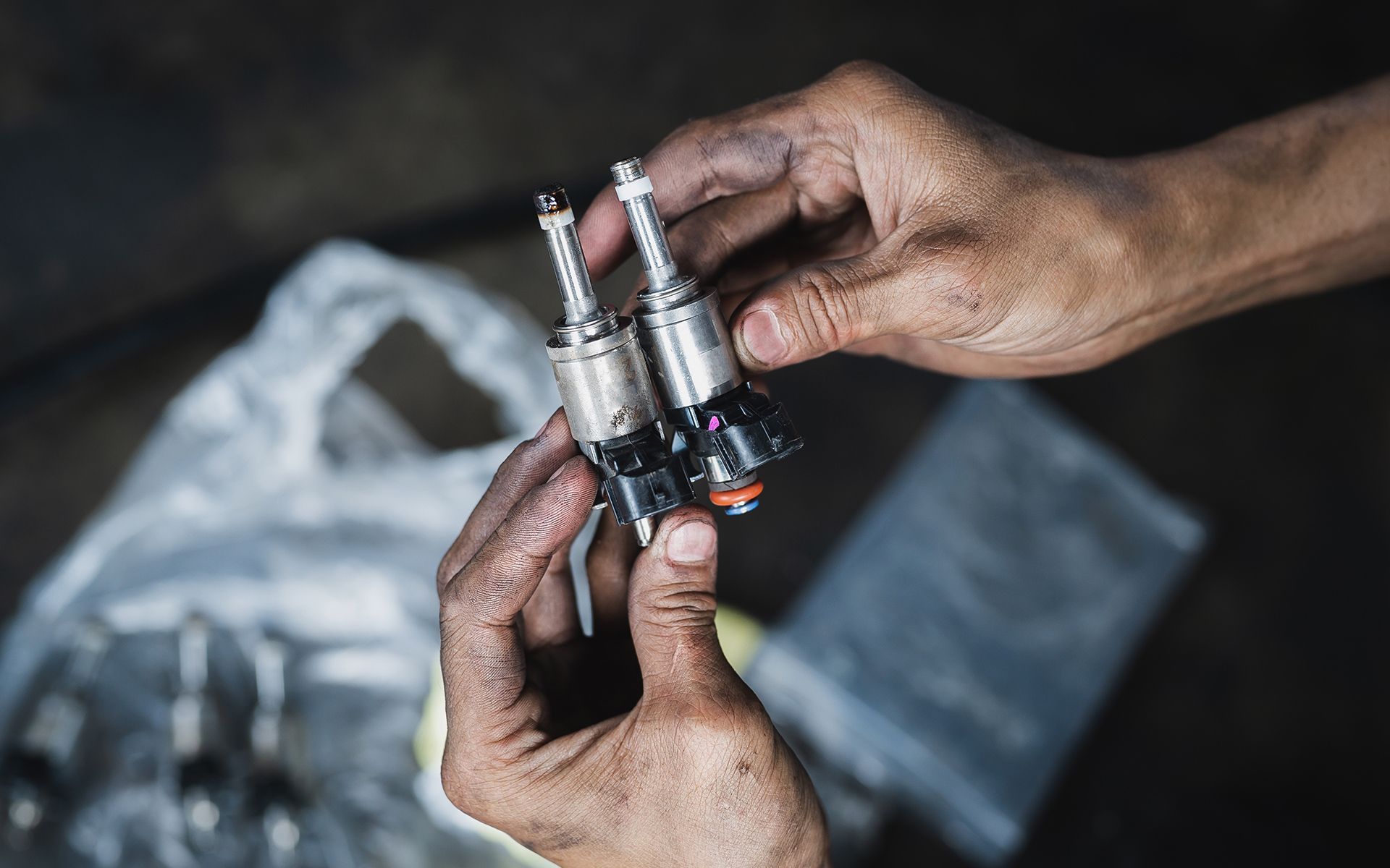 Hands holding two fuel injectors, likely automotive repair.