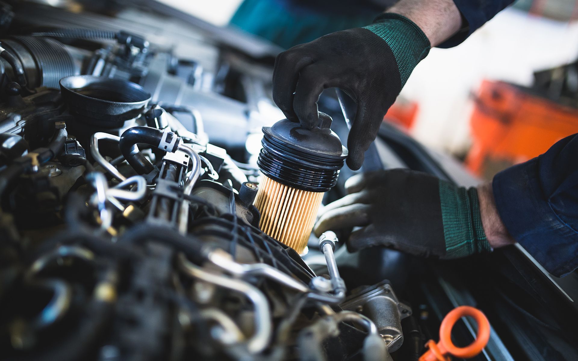 Mechanic replacing a car's oil filter, wearing gloves, engine visible.