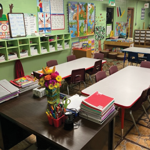A classroom with tables and chairs and a stack of red folders