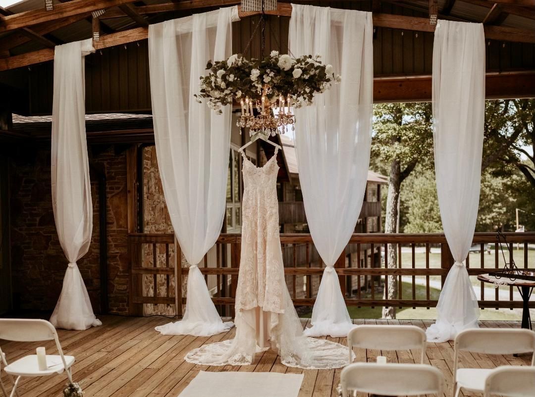 Rustic wedding ceremony setup with white draped fabric and hanging floral arrangement under a wooden pavilion