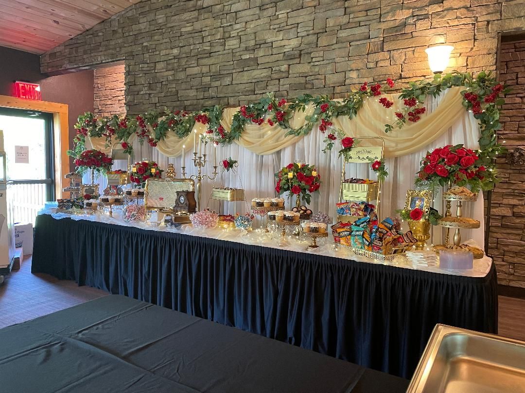 Decorated dessert buffet table with flowers and garlands against a stone wall in an event venue