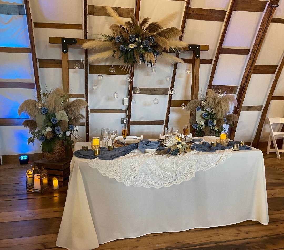 Decorated banquet table with white lace cloth, candles, and floral arrangements in a rustic wooden hall