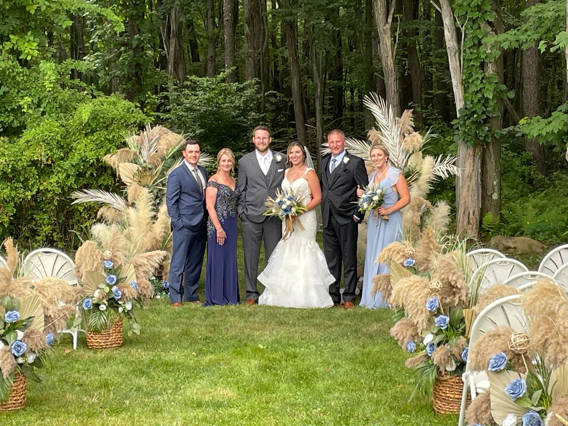 Wedding party posing outdoors on a decorated garden aisle with trees and white chairs