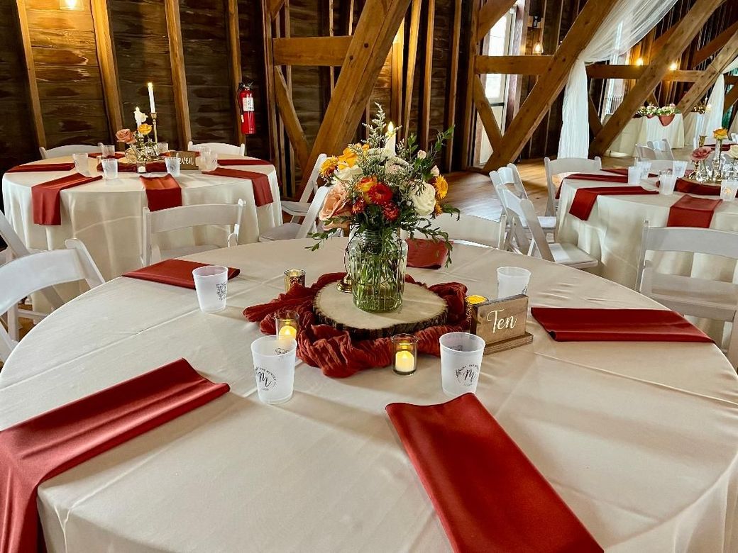 Round banquet tables with white tablecloths, red napkins, and floral centerpieces in a rustic event hall