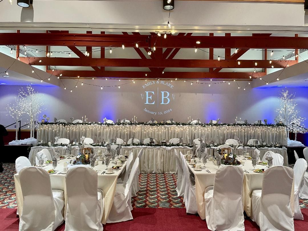 Elegant banquet hall with white chairs, long tables, blue uplighting, and a red patterned carpet.