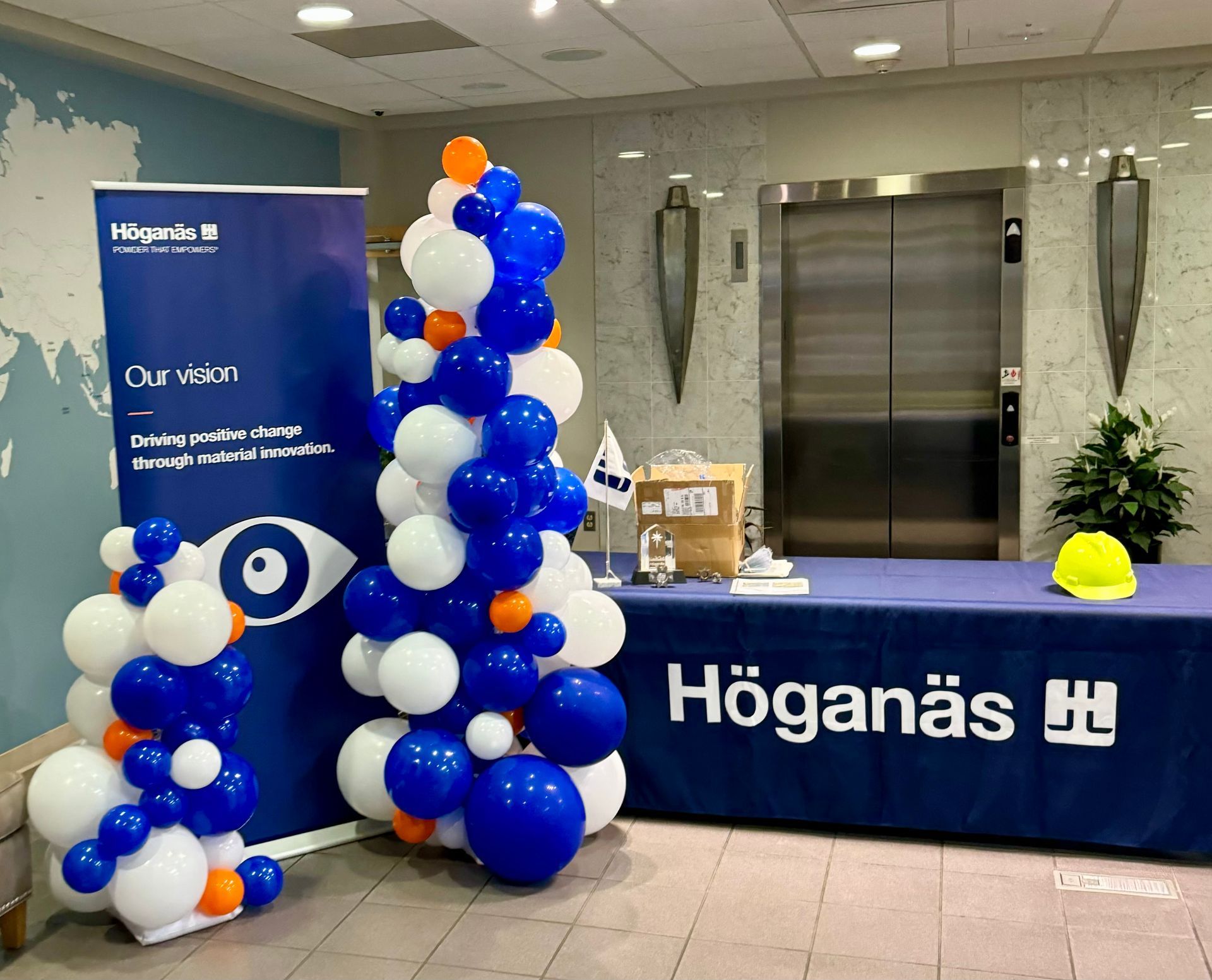 Höganäs event booth with blue-and-white balloon columns and a branded table at a lobby display